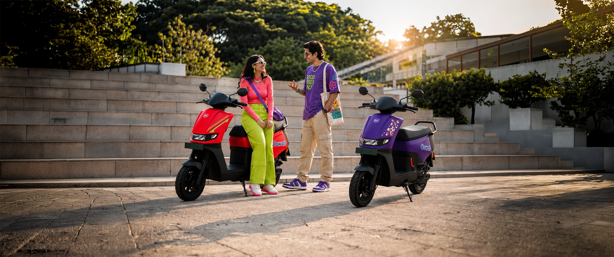 Two riders beside a red and a purple BG Oowah electric scooter